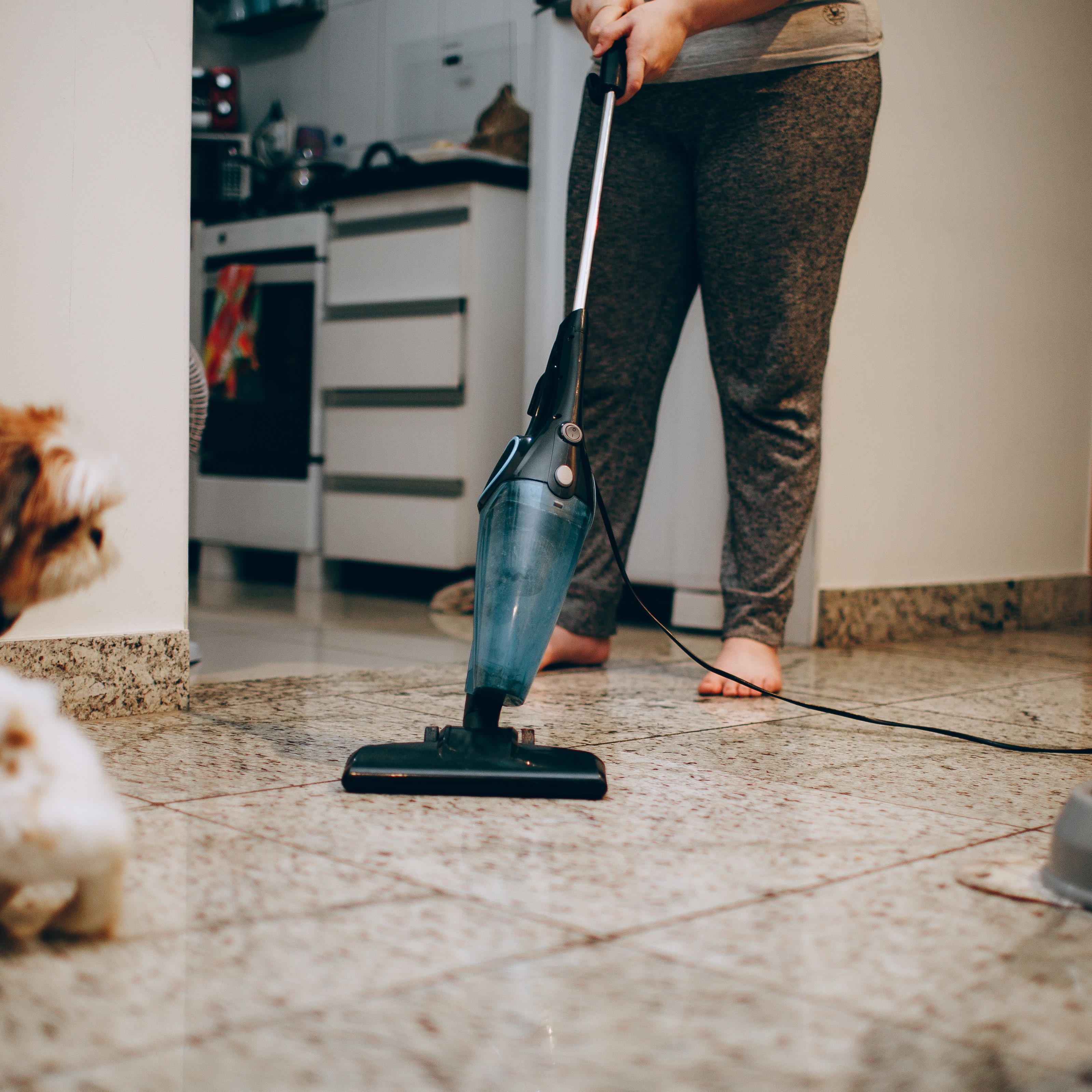 House cleaning professional vacuuming a tiled kitchen floor in a residential home